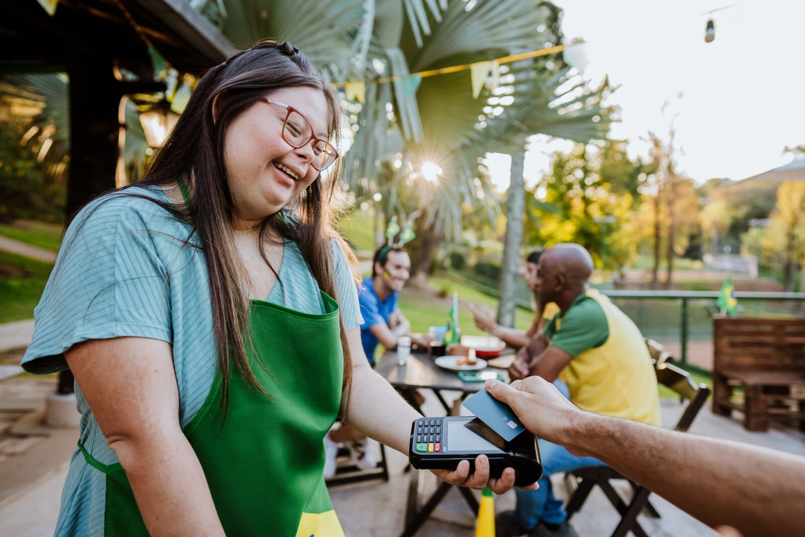 Bartender with Down Syndrome presents a payment terminal to a customer at his table