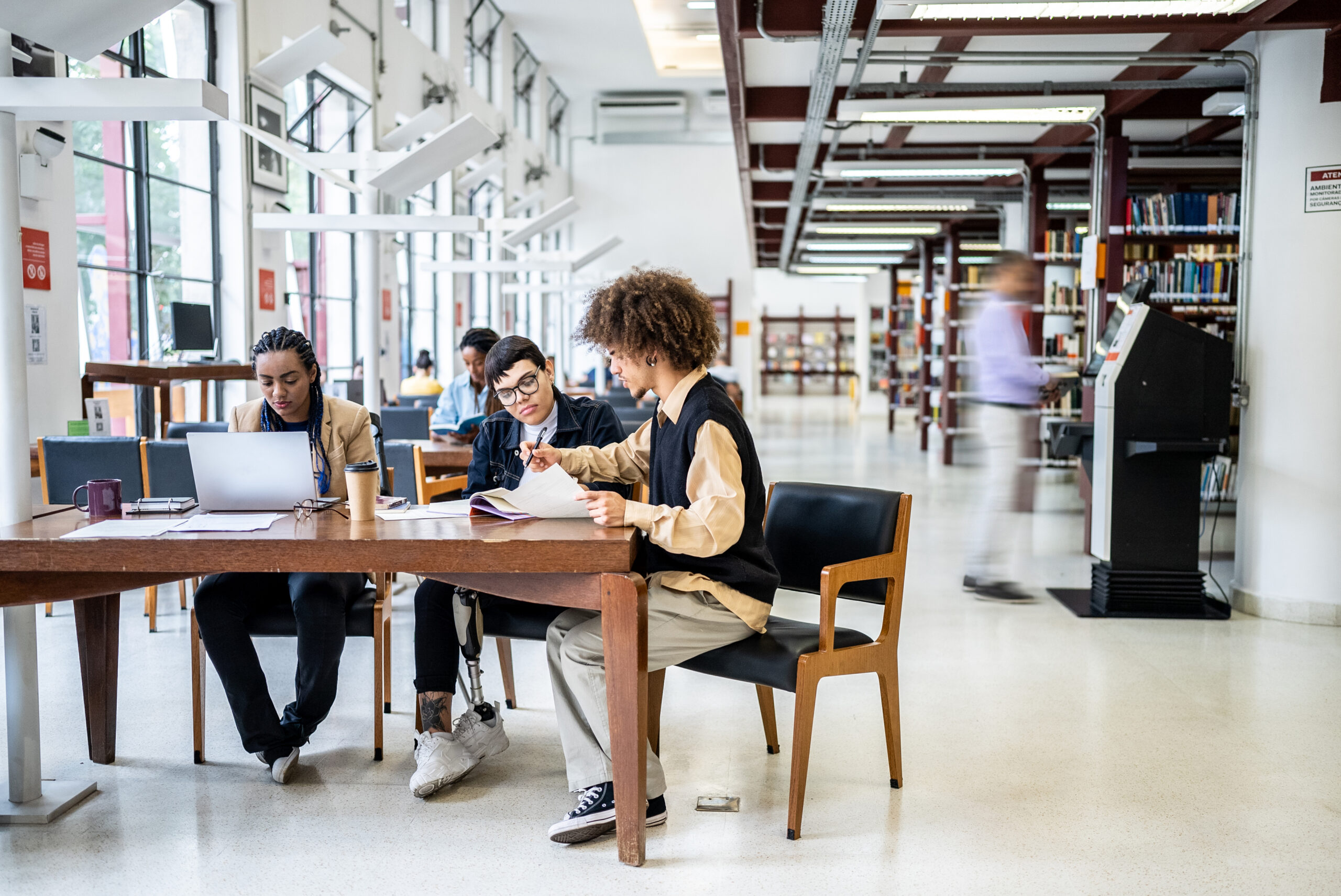 Three people sitting around a table studying in a university library. One student has a prosthetic leg.